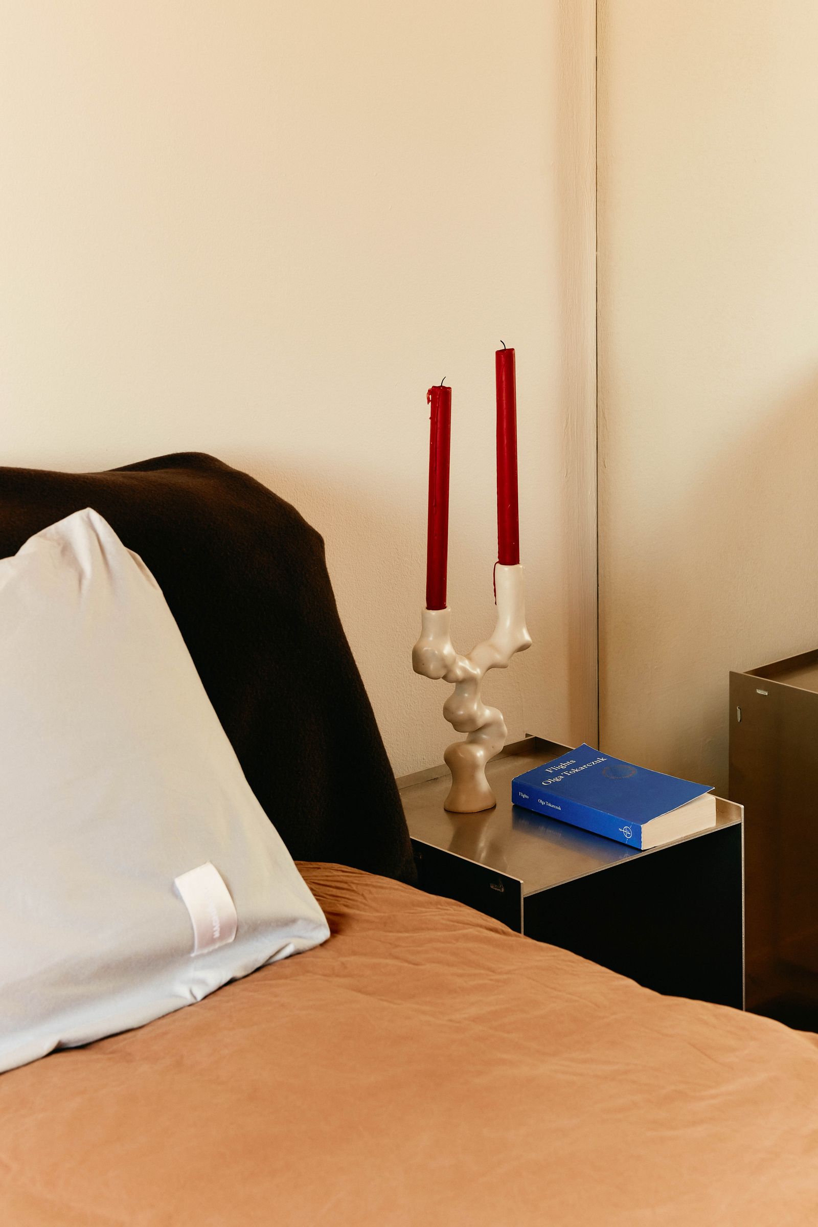 Neben dem Bett steht Tamara Romanovas „Akoya Double Candleholder“ auf einem FramaTisch. Bettwäsche von Magniberg.